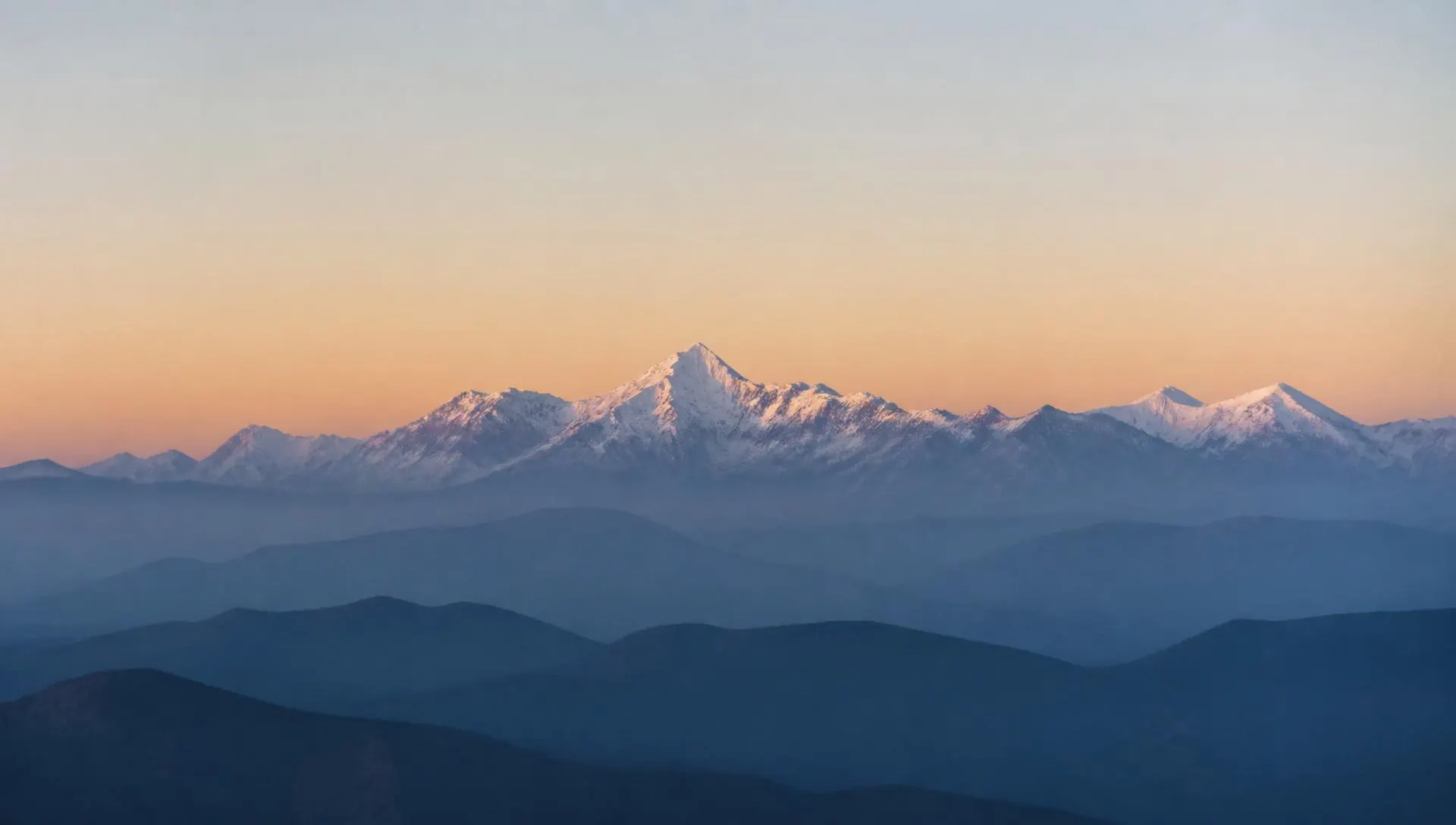 A distant snow-capped mountain range at dawn, ridgelines fading into haze